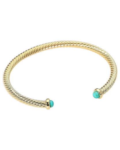 Gold cuff bracelet with turquoise beads on end and a white background.