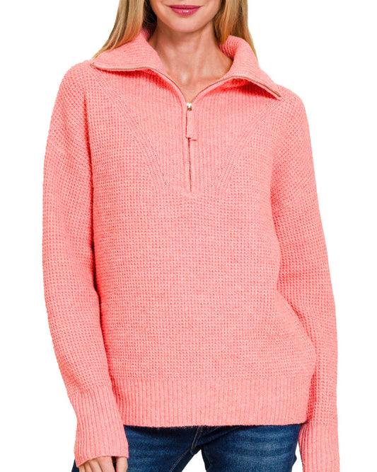 Woman wearing a bright peachy pink pullover sweater with a white background.