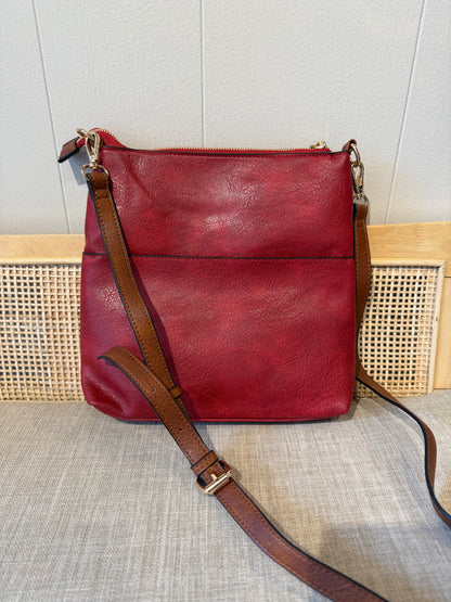 A burgundy leather shoulder crossbody bag with a brown leather strap and gold-tone hardware, displayed on a textured beige fabric surface.