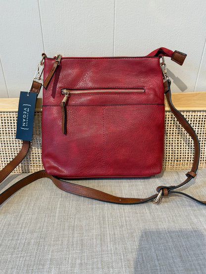 A red leather crossbody bag with brown leather straps and a front zip pocket, displayed on a woven bench with a brand tag visible.