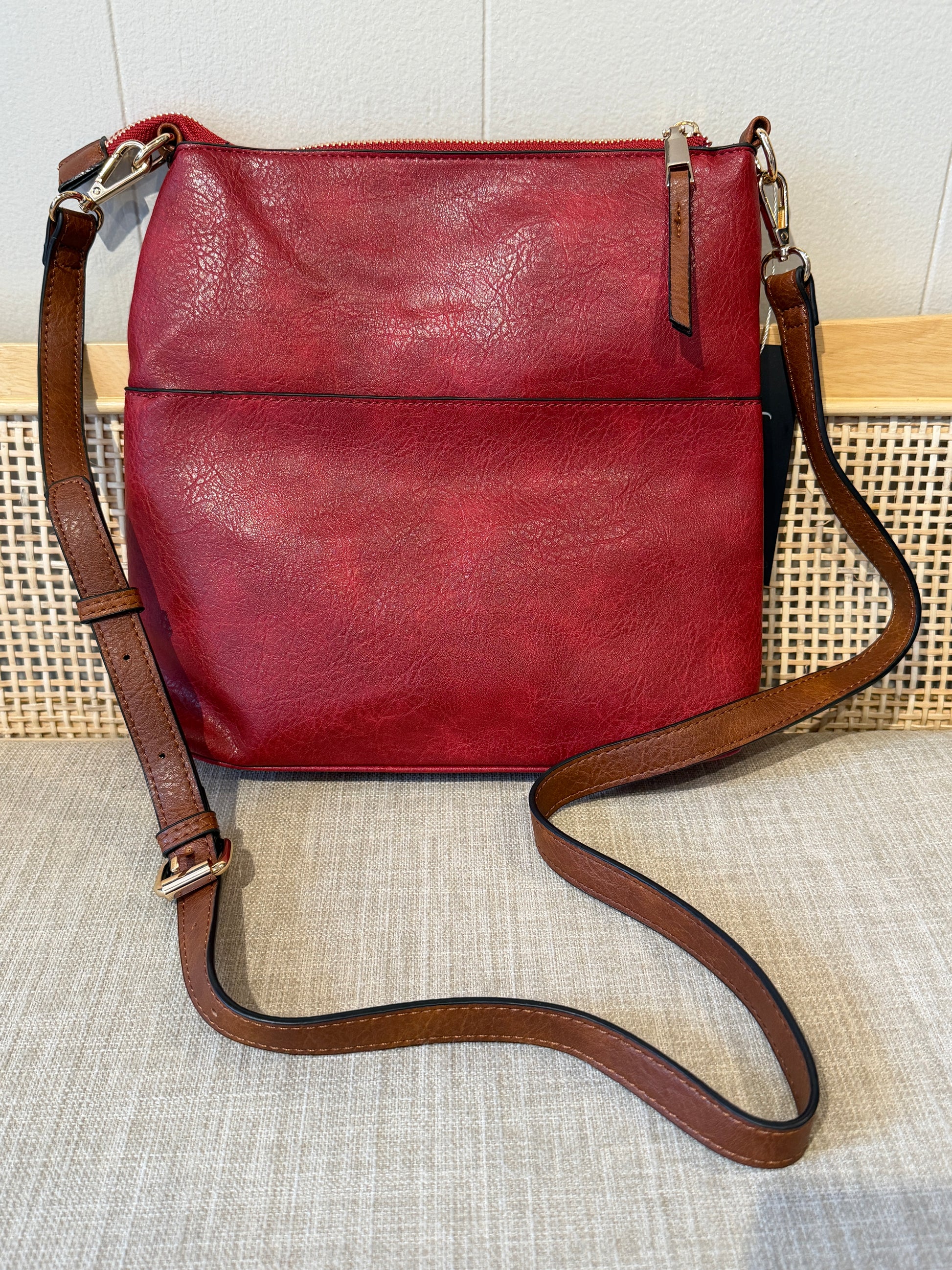 A burgundy leather shoulder crossbody bag with a brown leather strap and gold-tone hardware, displayed on a textured beige fabric surface.