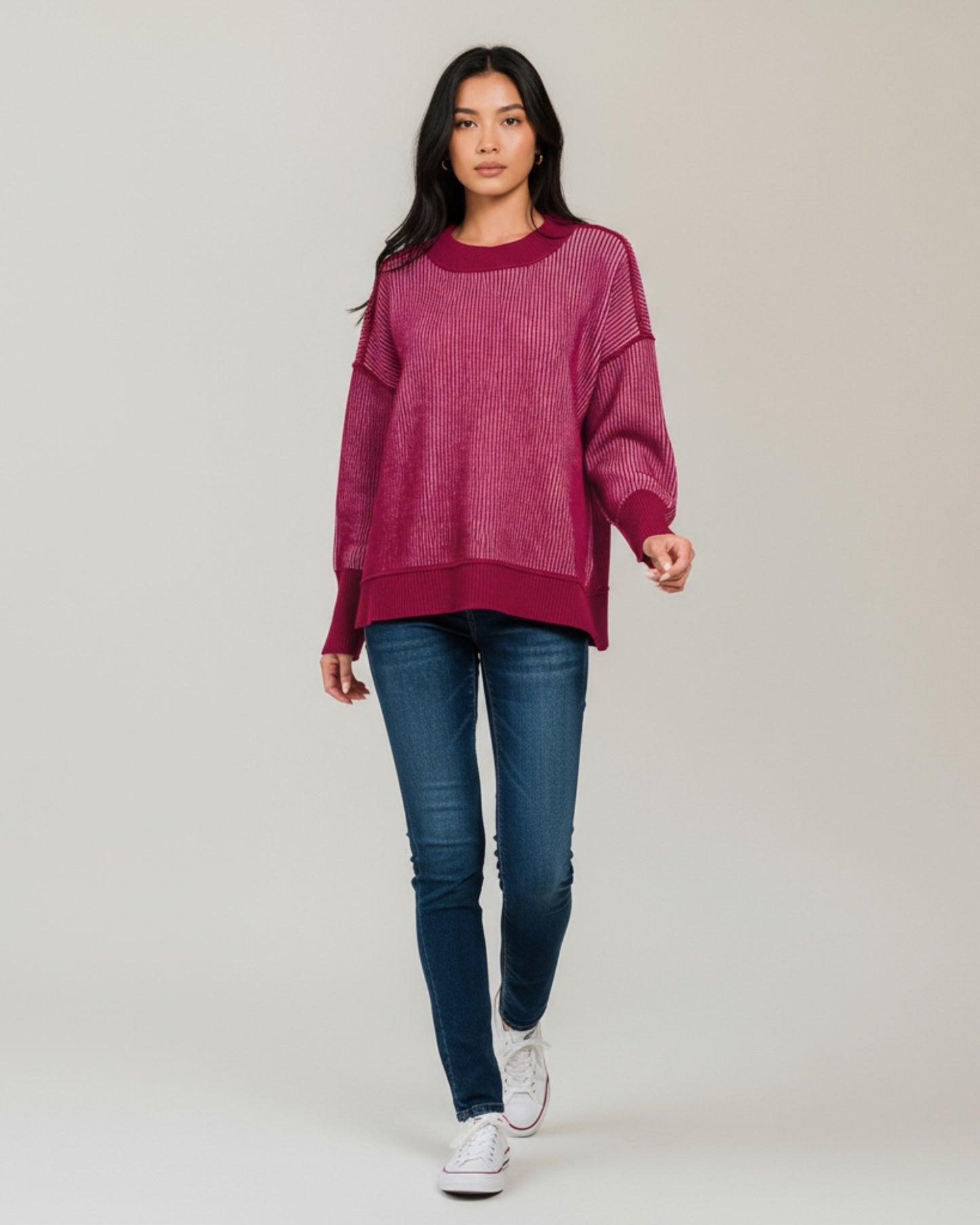 Woman wearing a burgundy sweater and blue jeans on a grey background.