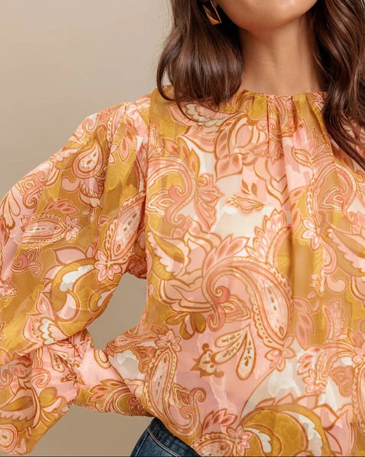 Woman wearing a patterned blouse with long sleeves against a neutral background.