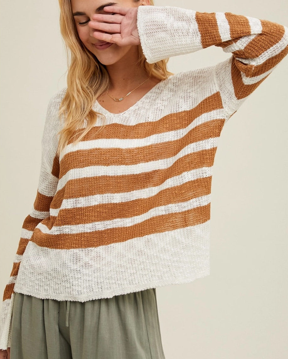 Woman wearing a striped sweater with brown and white colors on a plain background.