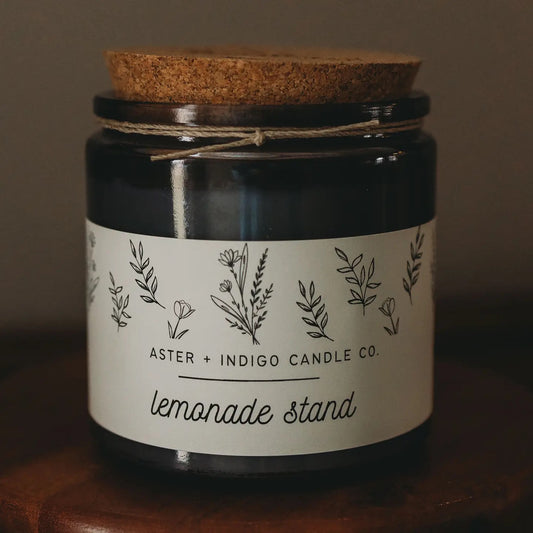 Aster + Indigo 12oz soy candle in a glass jar with cork lid, hand-poured and eco-friendly, available in various scents.