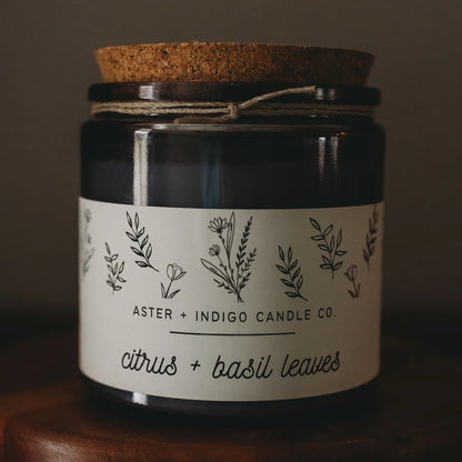 Aster + Indigo 12oz soy candle in a glass jar with cork lid, hand-poured and eco-friendly, available in various scents.