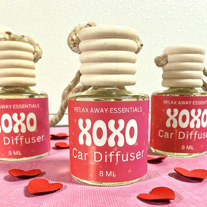 XOXO Car Diffuser bottles with pink labels on a pink background with red heart shapes.