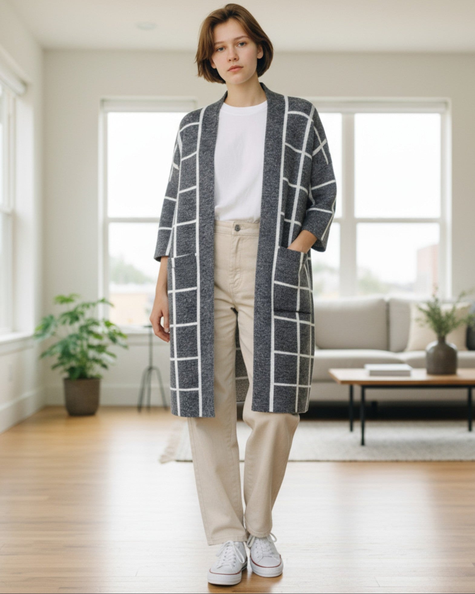 Person wearing a long, grey and white grid pattern cardigan in a bright living room. 