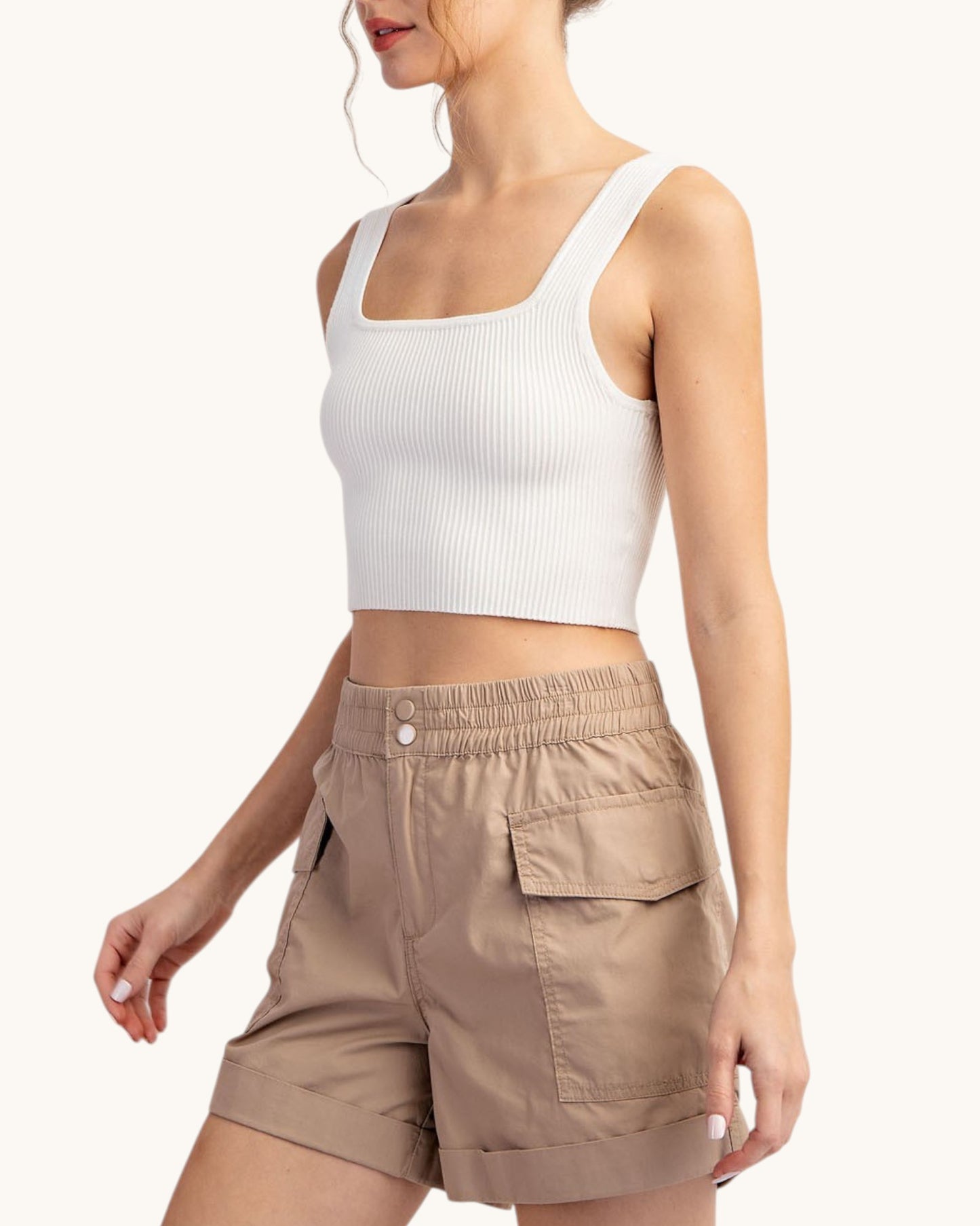 Woman wearing a white tank top and taupe cargo shorts on a white background.