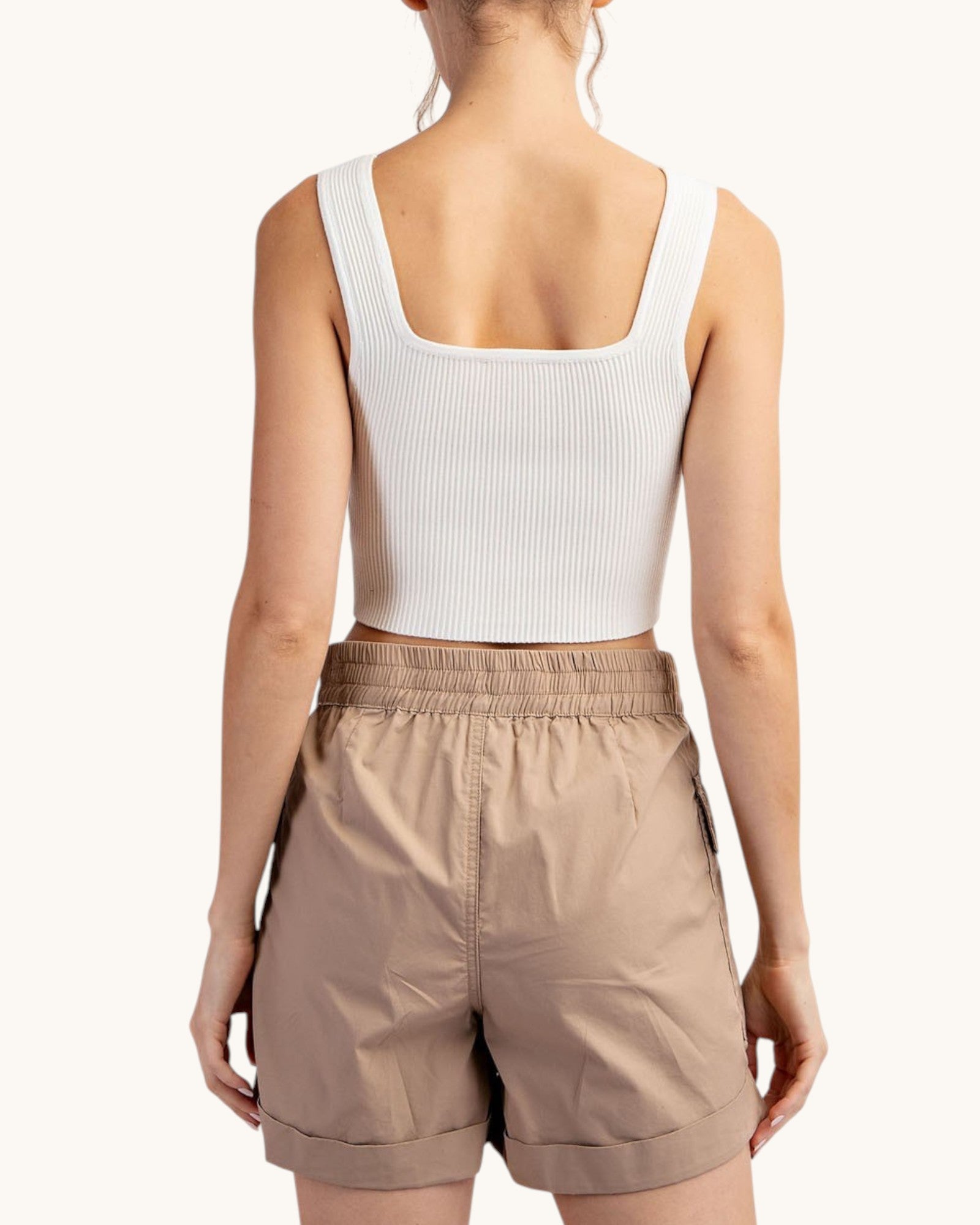 Woman wearing a white tank top and taupe cargo shorts on a white background.