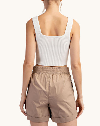 Woman wearing a white tank top and taupe cargo shorts on a white background.