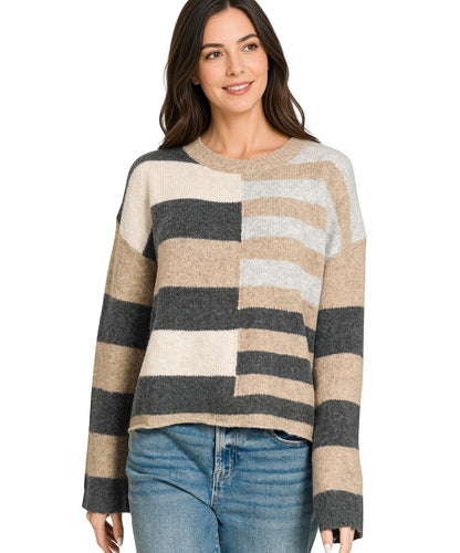 A woman wearing a fuzzy knit sweater with wide horizontal stripes in beige, charcoal, and light gray, paired with blue jeans, against a plain white background.