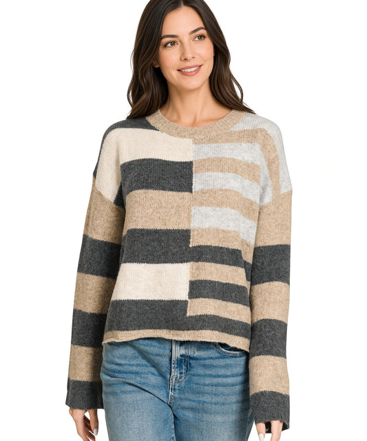 A woman wearing a fuzzy knit sweater with wide horizontal stripes in beige, charcoal, and light gray, paired with blue jeans, against a plain white background.