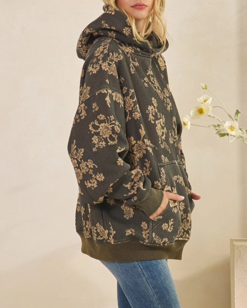 Woman wearing a floral hoodie and jeans in a neutral setting.
