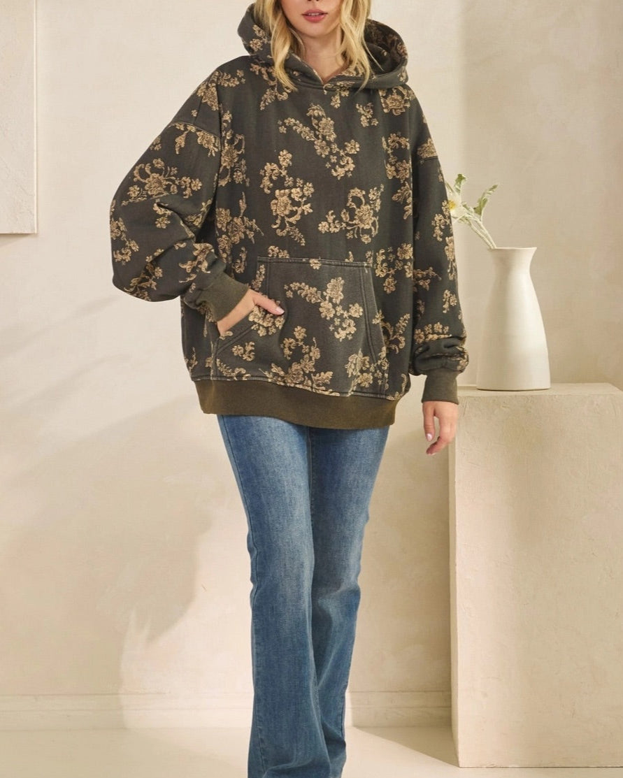 Woman wearing a floral hoodie and blue jeans standing in a minimalistic room.