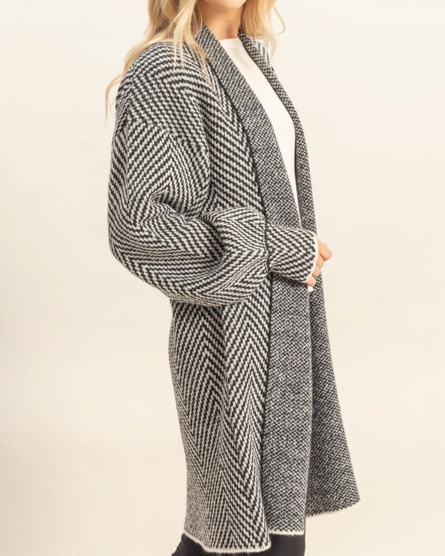 Woman wearing a long, patterned black and white coat on a white background.