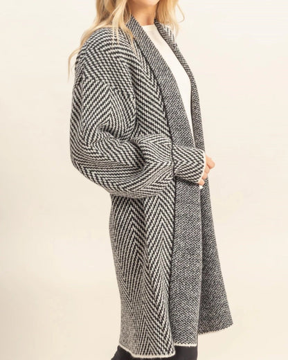Woman wearing a long, patterned black and white coat on a white background.