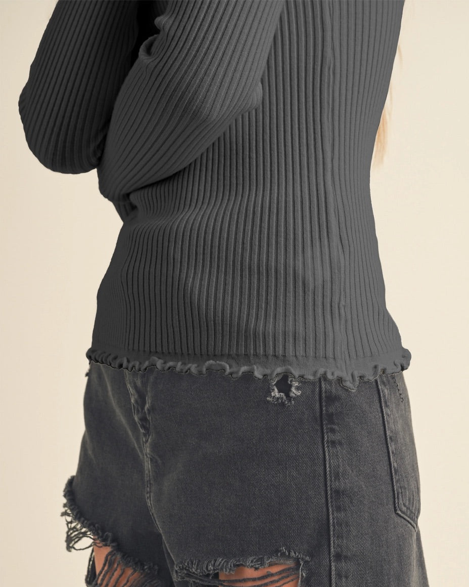 Bottom of a charcoal ribbed top and distressed black denim skirt on a beige background.