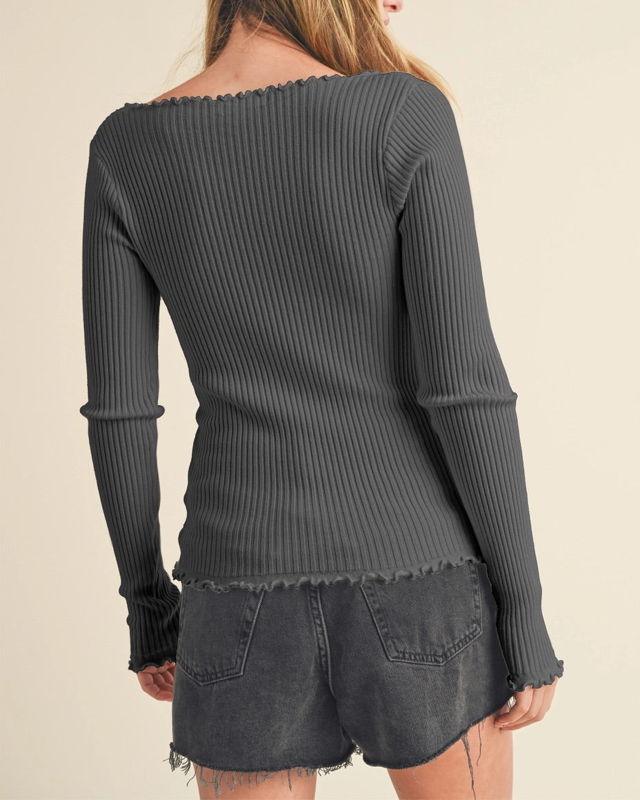 Woman wearing a slim fit dark gray ribbed long sleeve shirt with lettuce trim against a beige background.