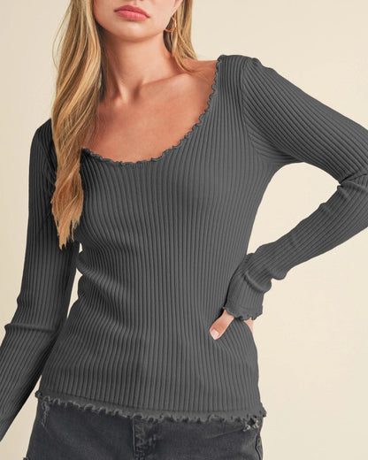 Woman wearing a slim fit dark gray ribbed long sleeve shirt with lettuce trim against a beige background.