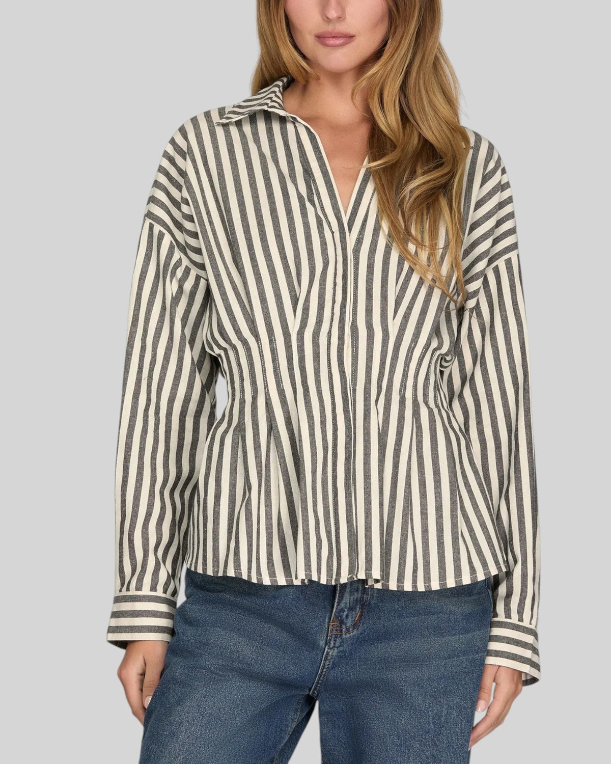 Model wearing a long sleeve charcoal and ivory button up with front waist pintucks and blue denim jeans. 