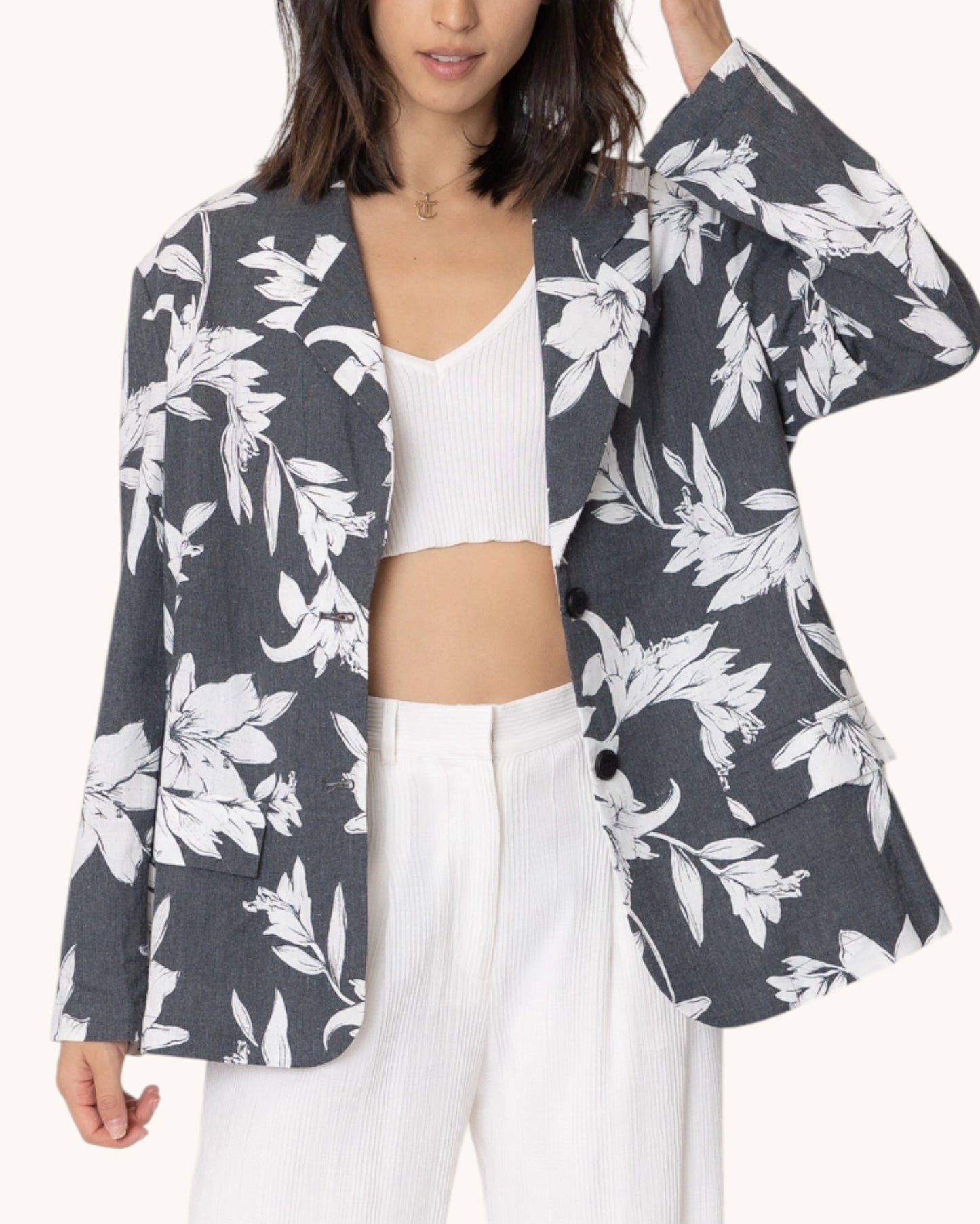Woman wearing a charcoal floral patterned blazer over a white tank top and paired with white dress pants.