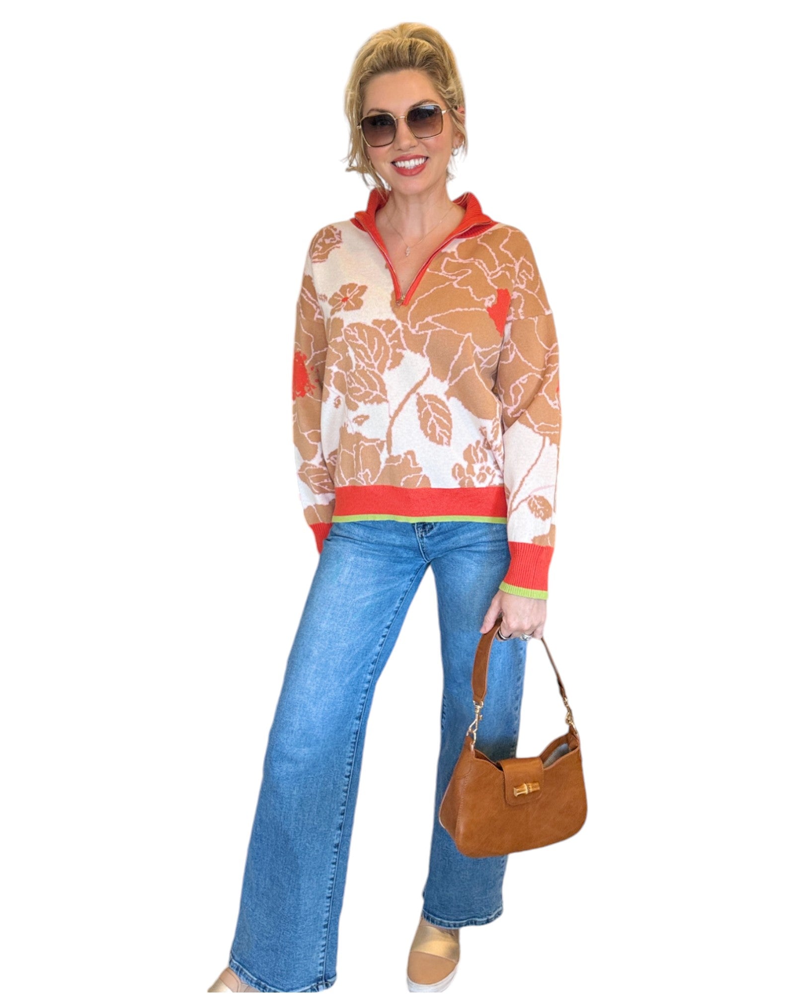 Woman wearing a coral, tan and cream half zip floral pattern sweater and blue jeans. 