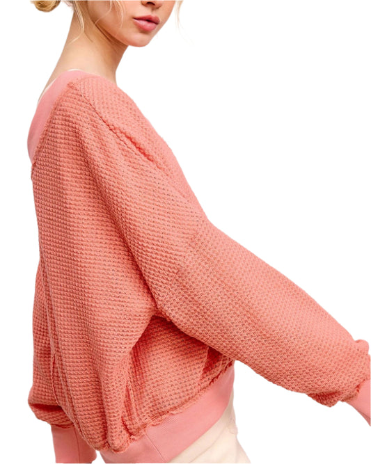 Peach coral waffle knit V-neck long sleeve top with relaxed fit and exposed seams.