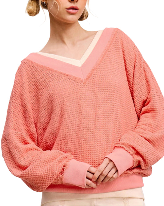 Woman wearing a peachy coral waffle knit V-neck long sleeve top with relaxed fit and exposed seams.