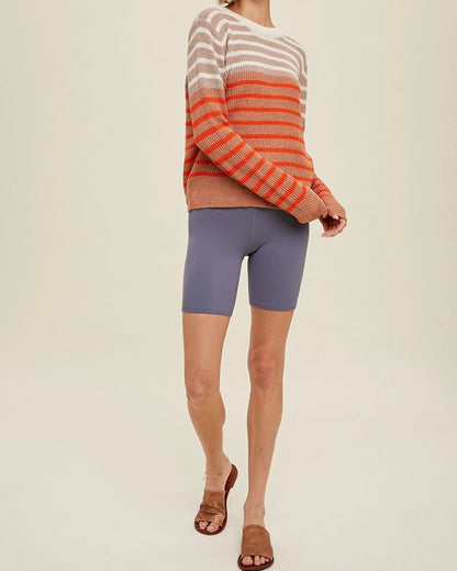 Woman wearing a striped sweater and bike shorts on a plain background