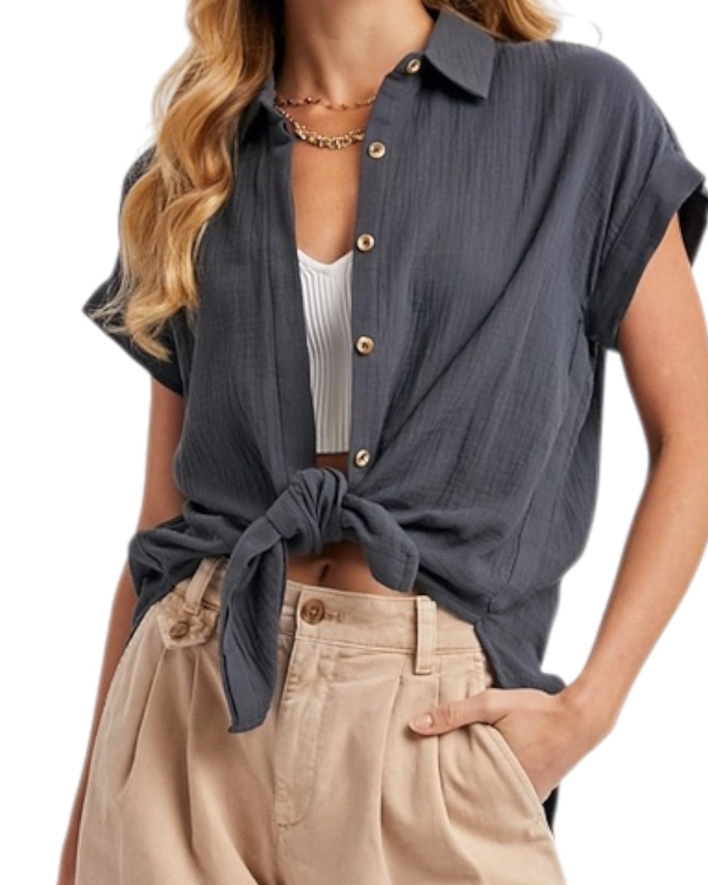 Woman wearing a tied dark blue grey shirt with beige pants on a white background.