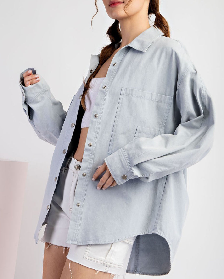 Woman wearing a light blue denim shirt jacket / shacket over a white top on a white background.