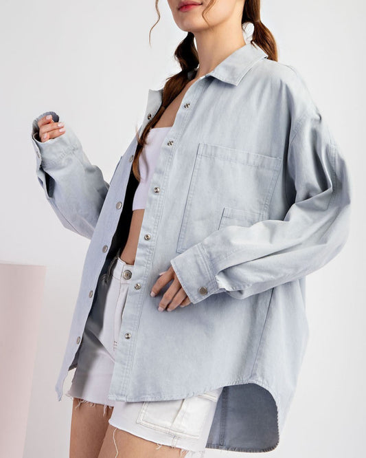 Woman wearing a light blue denim shirt jacket / shacket over a white top on a white background.