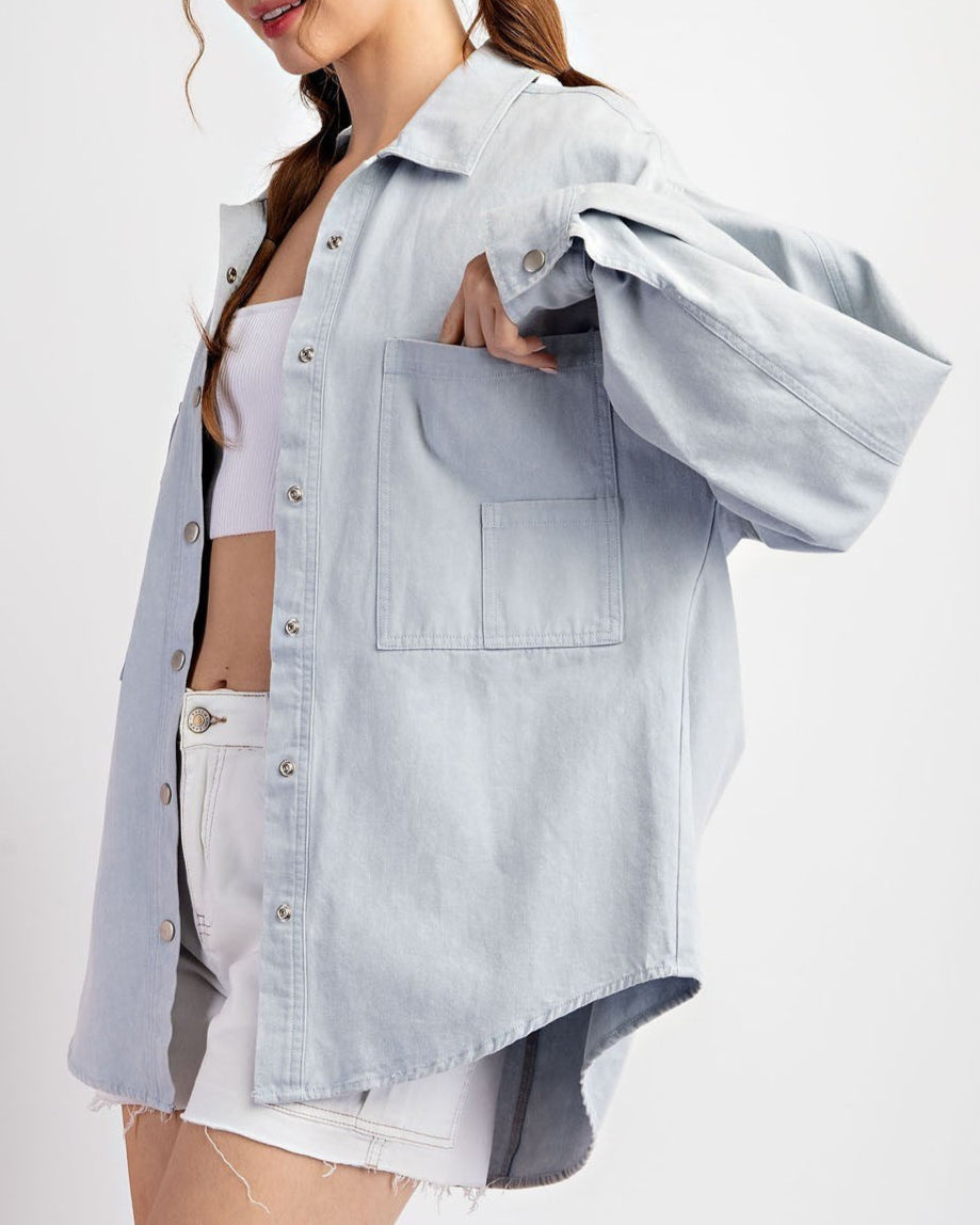 Woman wearing a light blue denim shirt jacket / shacket over a white top on a white background. 