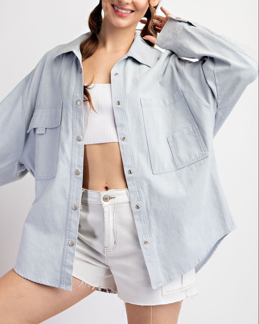 Woman wearing a light blue denim shirt jacket / shacket over a white top on a white background.