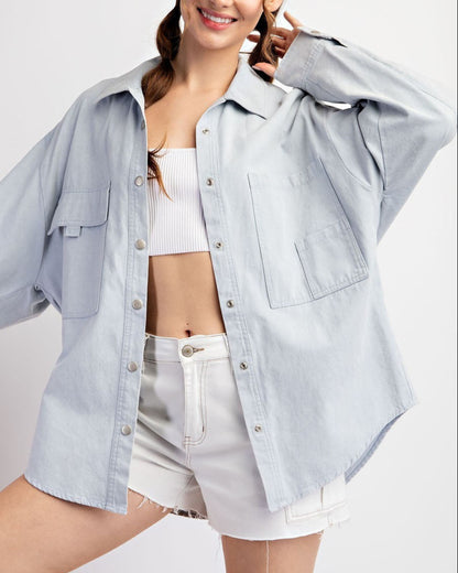 Woman wearing a light blue denim shirt jacket / shacket over a white top on a white background.
