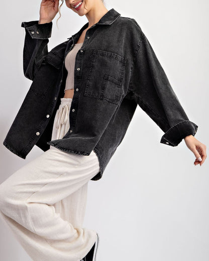 Woman wearing a black denim jacket / shacket over a beige top and white pants on a light gray background.