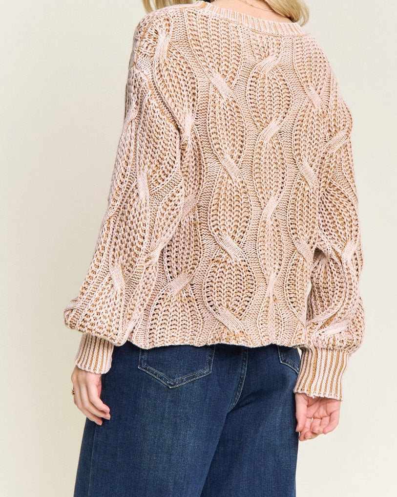 Woman wearing a beige knitted cotton sweater and blue jeans on a plain background.