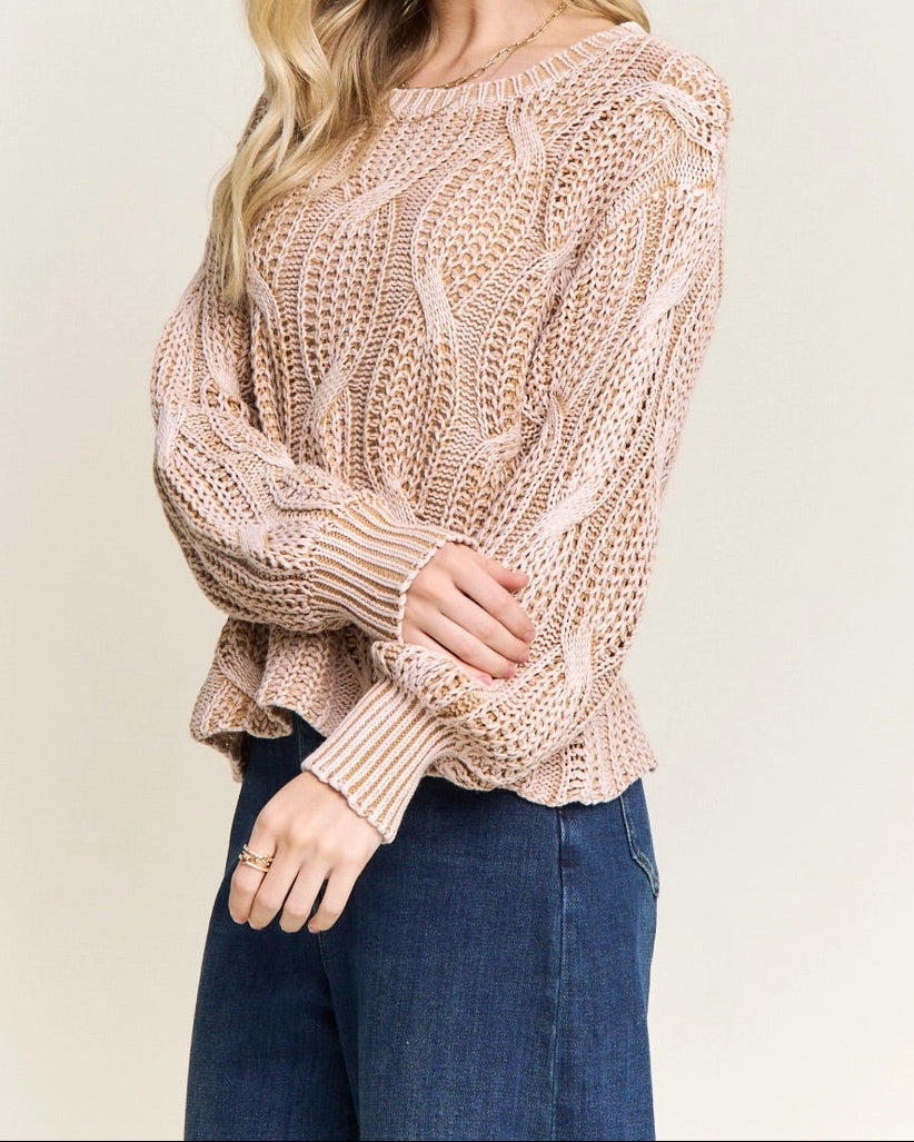 Woman wearing a beige knitted cotton sweater and blue jeans on a plain background.