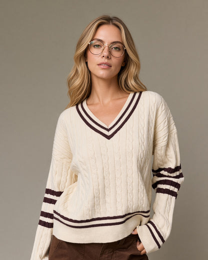 Model wearing a cream cable knit V-neck sweater with brown striped neckline, sleeves and hem.