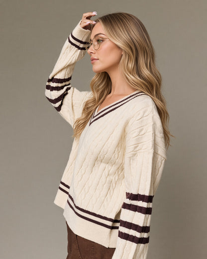 Side view model wearing a cream cable knit V-neck sweater with brown striped neckline, sleeves and hem.