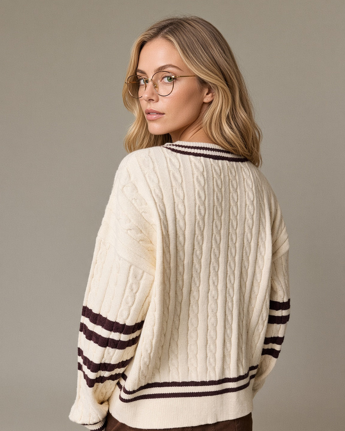 Back view of a model wearing a cream cable knit V-neck sweater with brown striped neckline, sleeves and hem.
