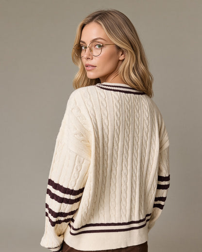 Back view of a model wearing a cream cable knit V-neck sweater with brown striped neckline, sleeves and hem.