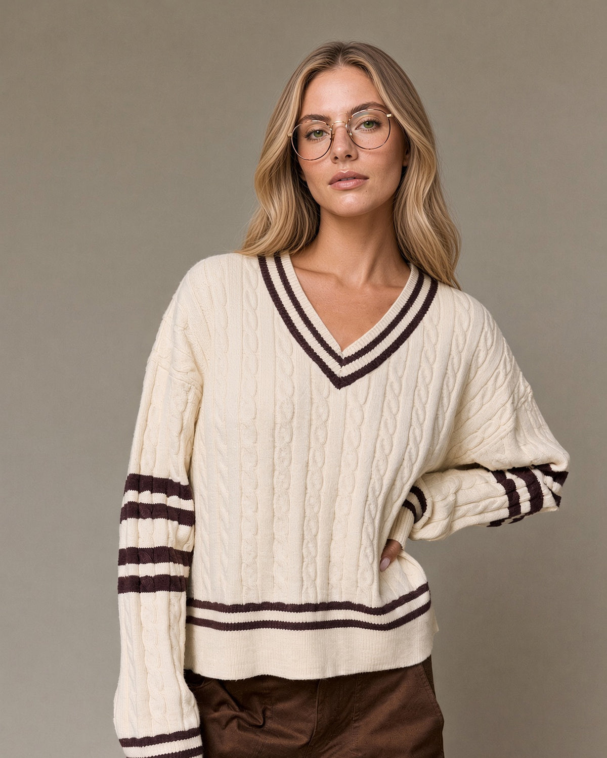 Model wearing a cream cable knit V-neck sweater with brown striped neckline, sleeves and hem.