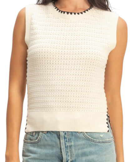 White sleeveless top with black trim worn by a person on a white background.