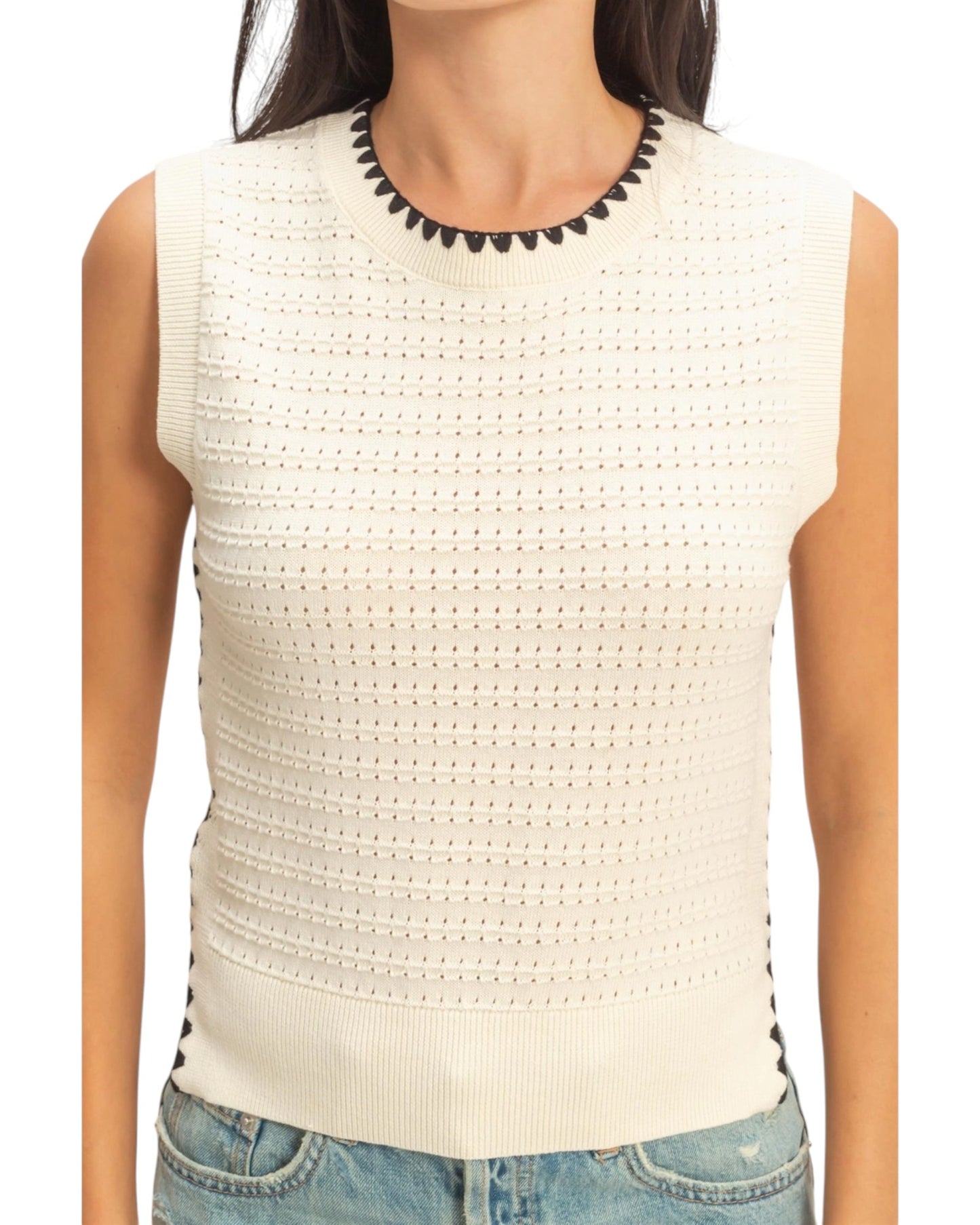 Cream knit sleeveless top with black trim accents worn by a person on a white background.