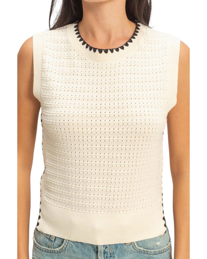 Cream knit sleeveless top with black trim accents worn by a person on a white background.