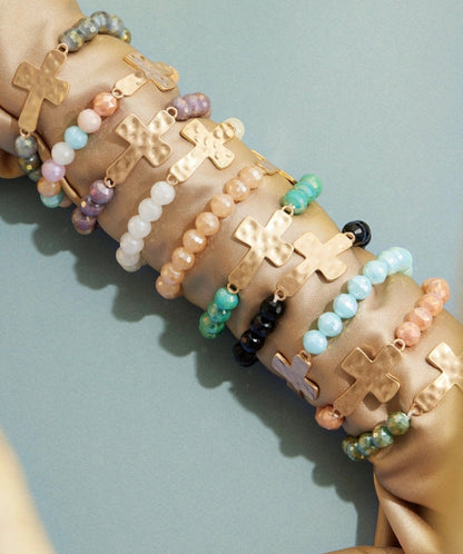 Close-up of different colored glass bead stretch bracelets featuring a hammered gold cross charm.