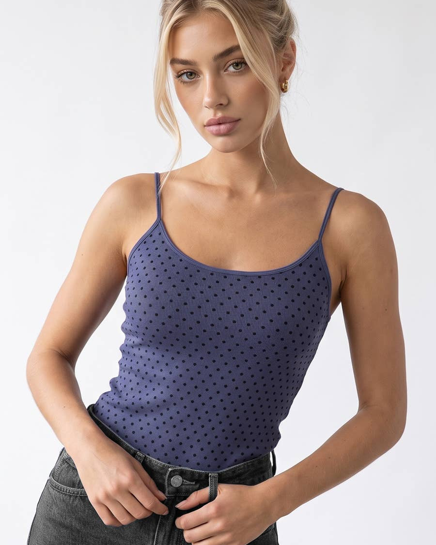 A woman modeling a sleeveless tank top top in a dusty royal blue color with a small black polka dot pattern, paired with dark gray jeans. 