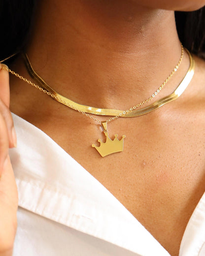 Gold necklace with a crown pendant worn by a person against a white background